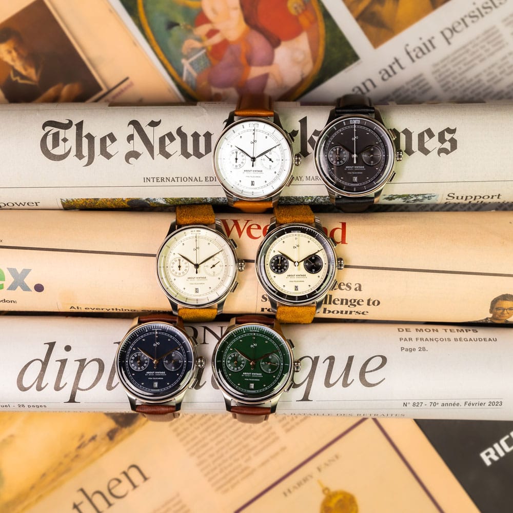 Six vintage-inspired chronograph watches with varied dark, cream and green dials arranged on open newspapers in an editorial horological setting