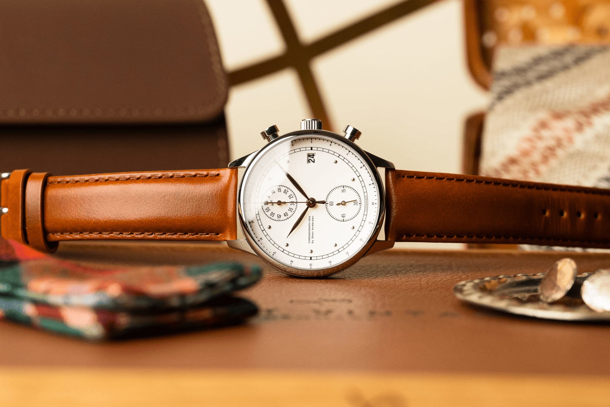 1834 Chronograph by AV86 with vintage-inspired dial, sapphire crystal, chronograph function, and brown leather strap on warm wood surface