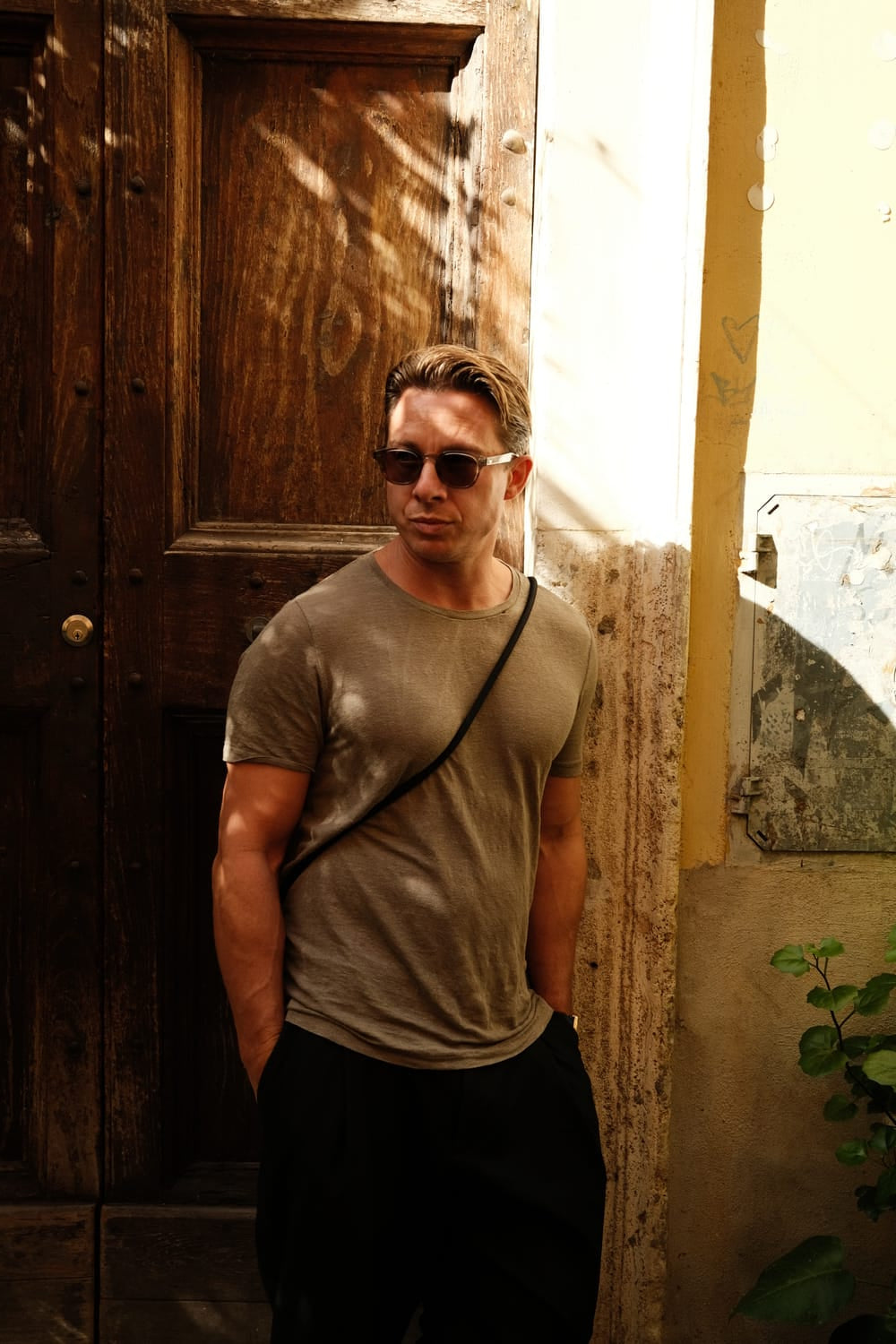 Man wearing casual muted tones and sunglasses standing in warm sunlight with Mediterranean backdrop, evoking vintage-inspired lifestyle for AV86 "1954 Amalfi Mechanical, Gold / Gold