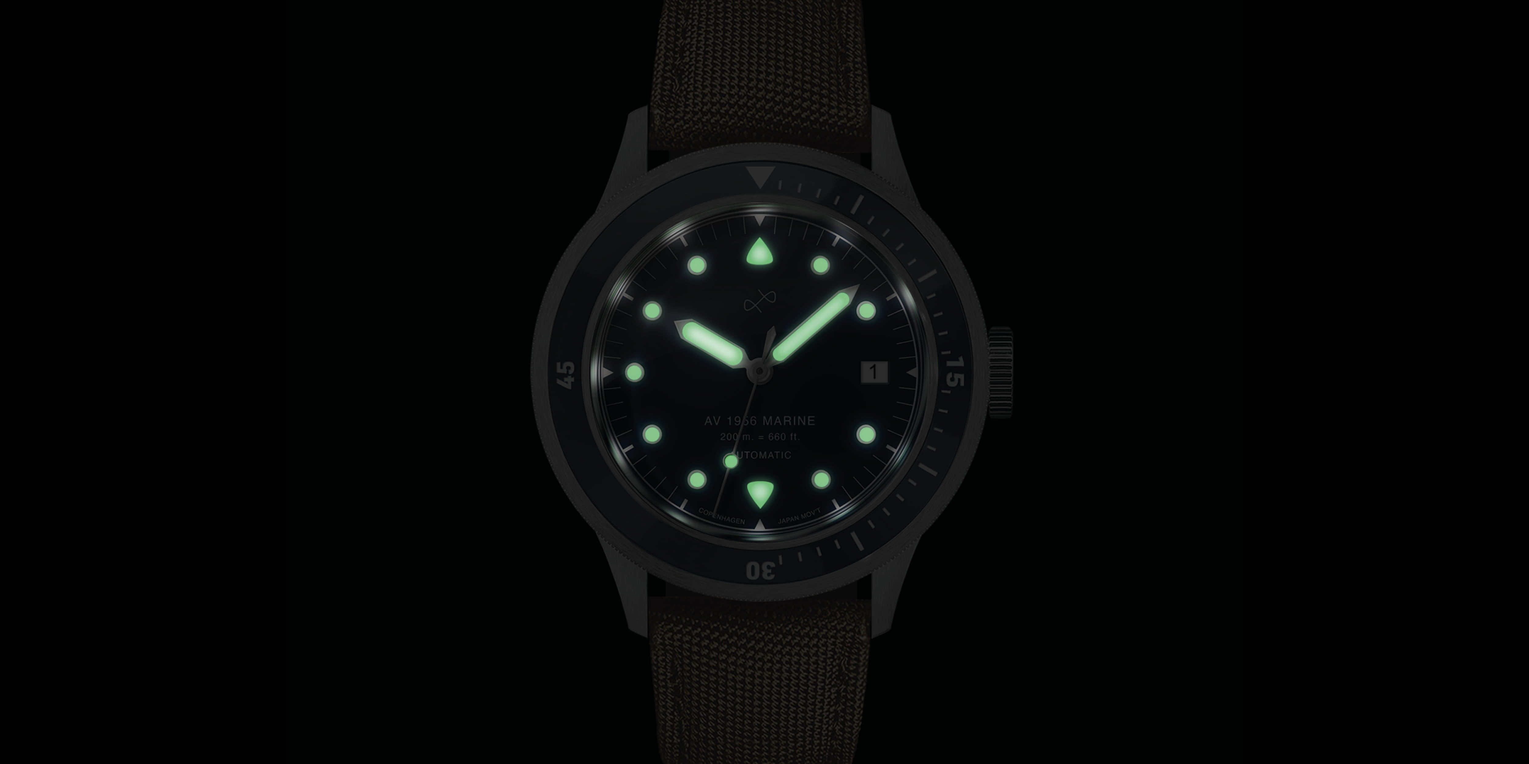 Vintage diver wristwatch glowing with luminescent markers, hands, and bezel on a textured dark brown strap.