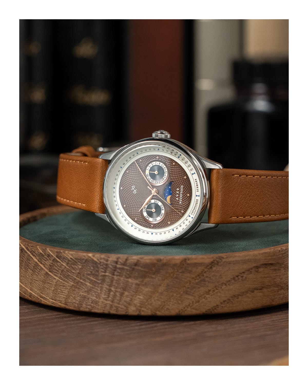 AV86 vintage-inspired automatic watch with textured dial, dual subdials, moonphase complication, and brown leather strap resting on wood tray