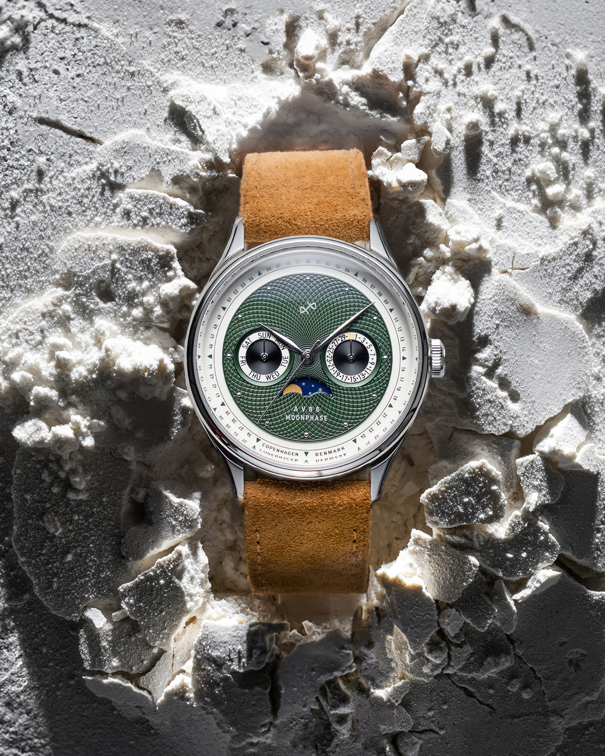 AV86 moonphase watch with green guilloché dial, sapphire crystal, moonphase complication, and tan suede leather strap resting on textured surface