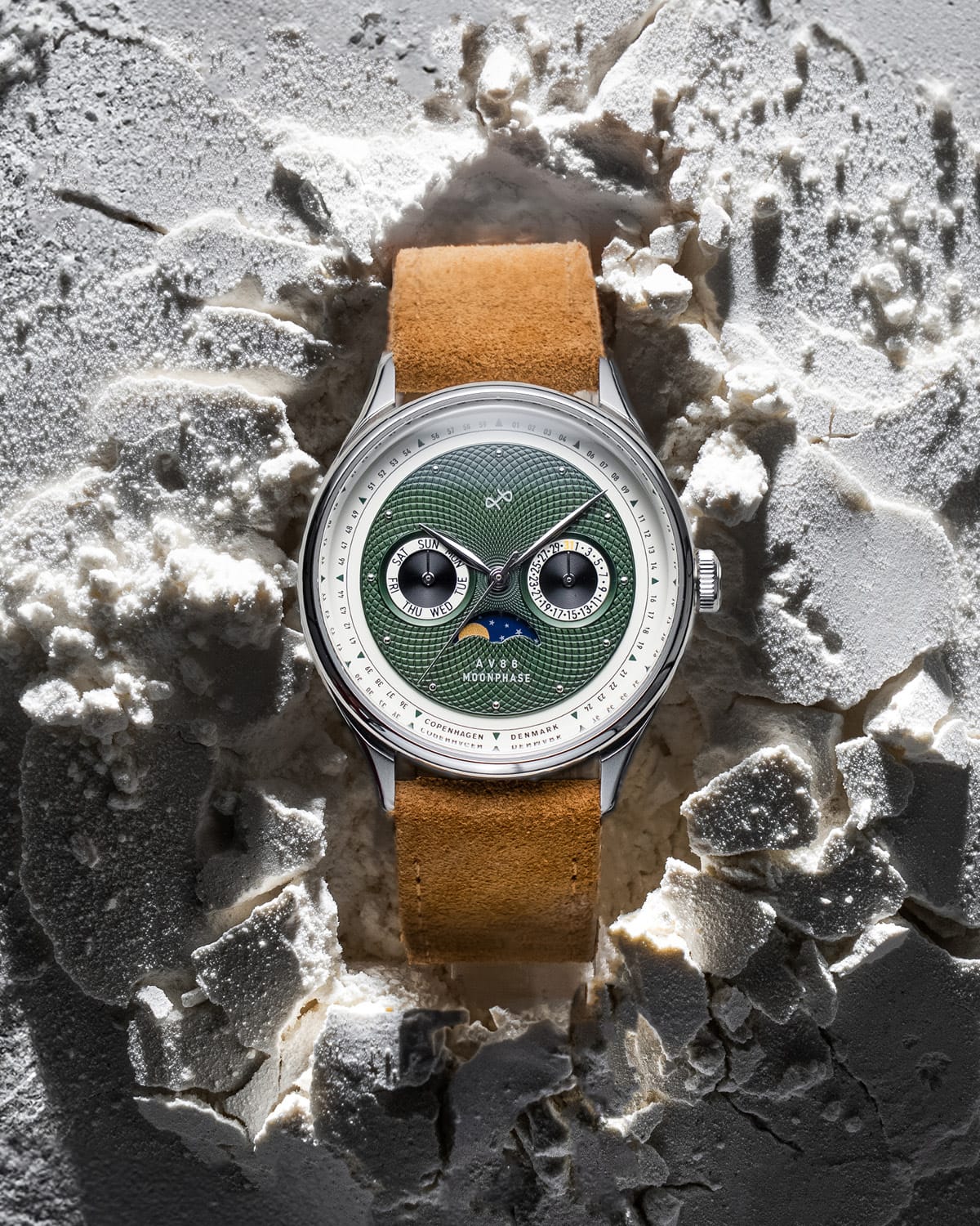 AV86 moonphase watch with green guilloché dial, sapphire crystal, moonphase complication, and tan suede leather strap resting on textured surface