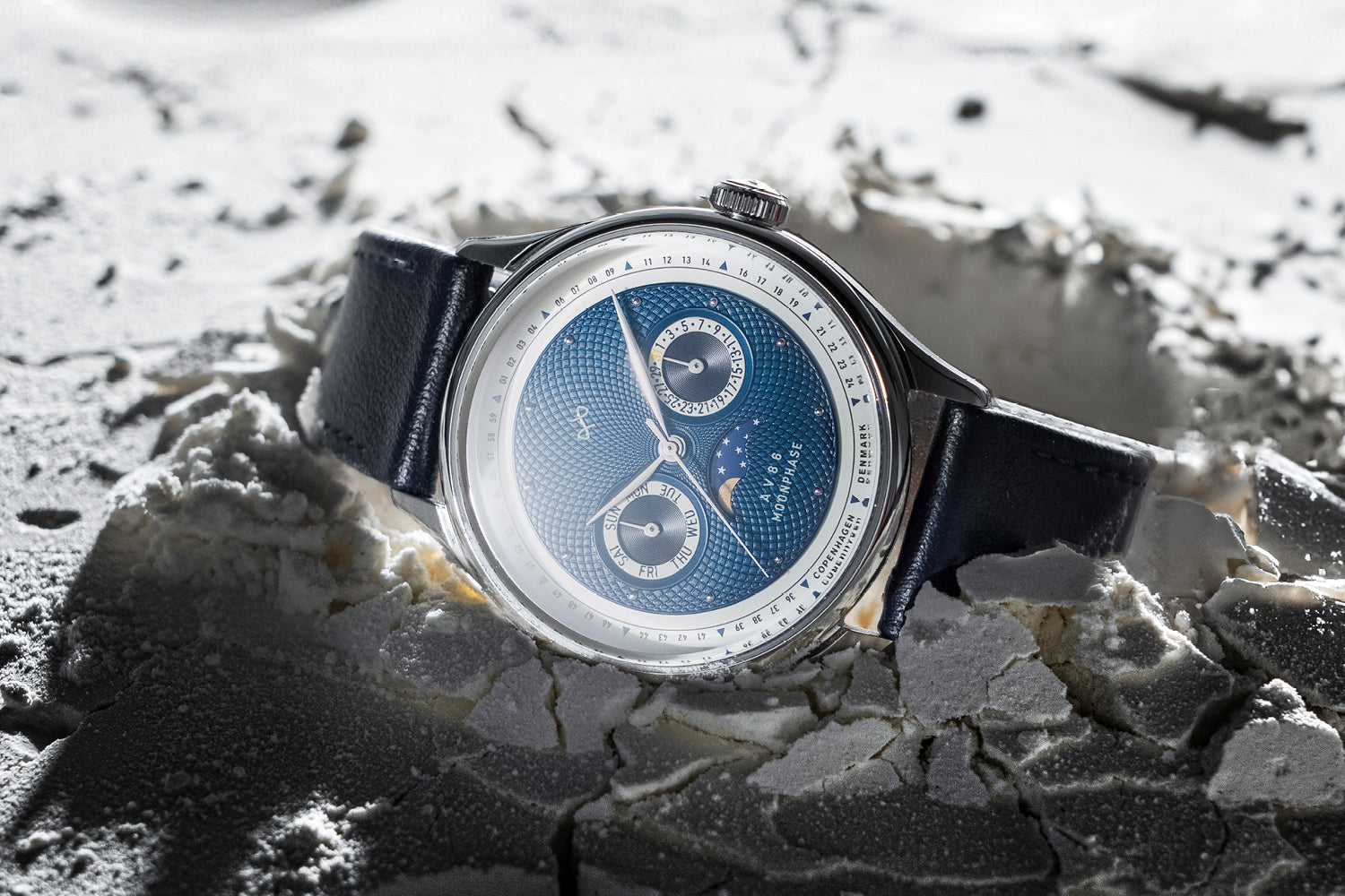 AV86 chronograph with sapphire crystal, textured dial, moonphase complication, and black leather strap on cracked surface background