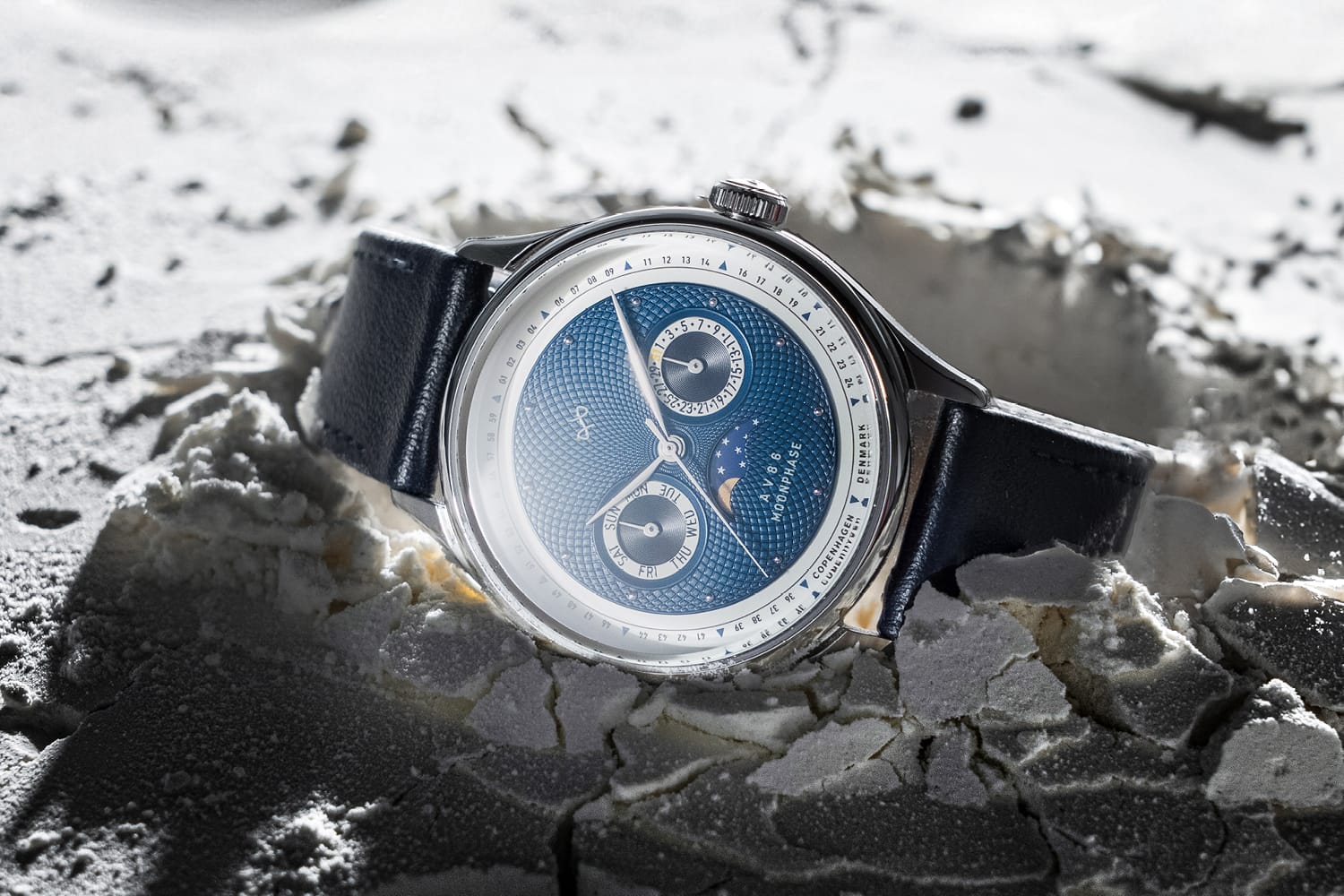AV86 chronograph with sapphire crystal, textured dial, moonphase complication, and black leather strap on cracked surface background