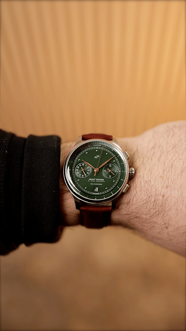 AV86 vintage-inspired chronograph with green dial, twin subdials, polished case and brown leather strap worn against a wood backdrop