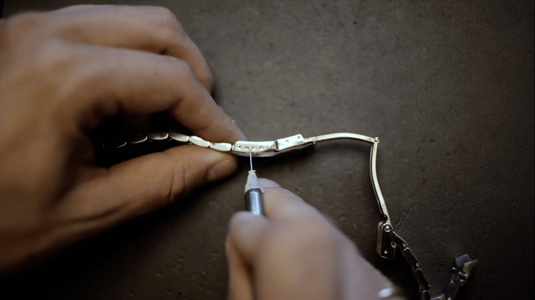Watchmaker’s hands adjusting a polished metal watch bracelet with a precision tool on a dark workbench, highlighting meticulous craftsmanship