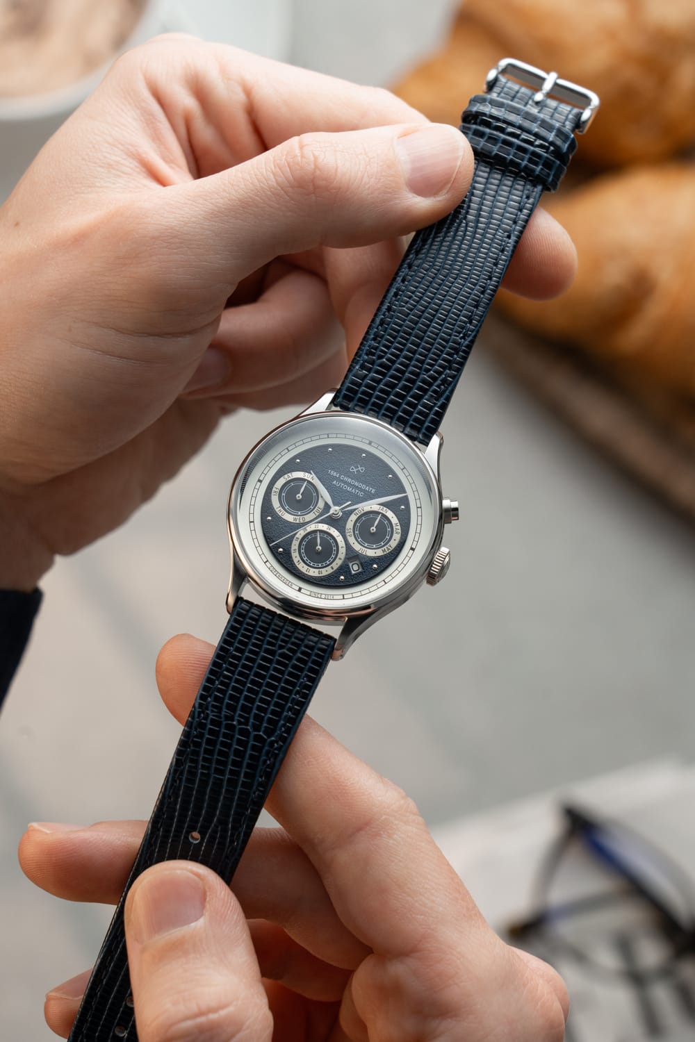 1564 Chronodate Automatic by AV86 features a vintage-inspired automatic chronograph with a textured dial, triple subdials, polished case, and a deep blue patterned leather strap, reflecting refined Danish horological craftsmanship and Nordic minimalism.