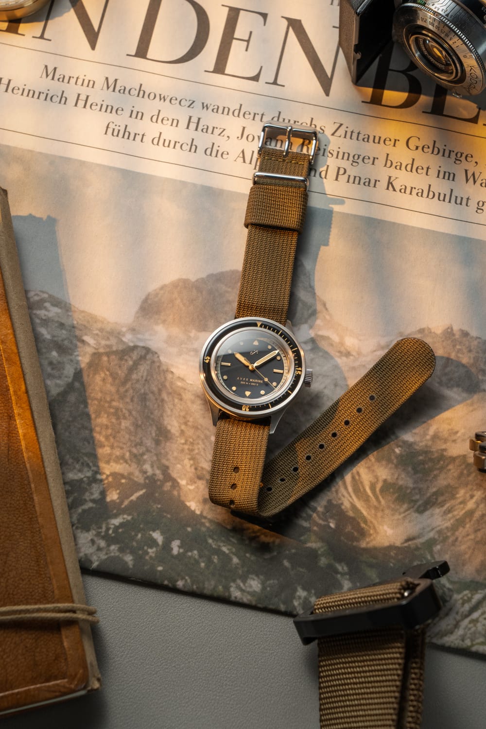 1956 Marine von AV86: Vintage-inspirierte Taucheruhr mit Saphirglas, Kompass-Lünette und strukturiertem Stoff-Armband vor Zeitungshintergrund