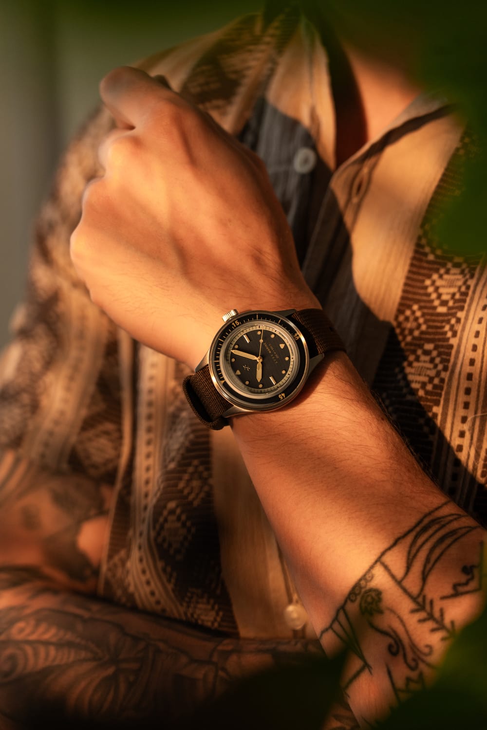 1956 Marine von AV86 – eine vom Vintage-Stil inspirierte Taucheruhr mit Saphirglas, Kompasslünette und strukturiertem Kautschukarmband am Handgelenk in warmem Licht