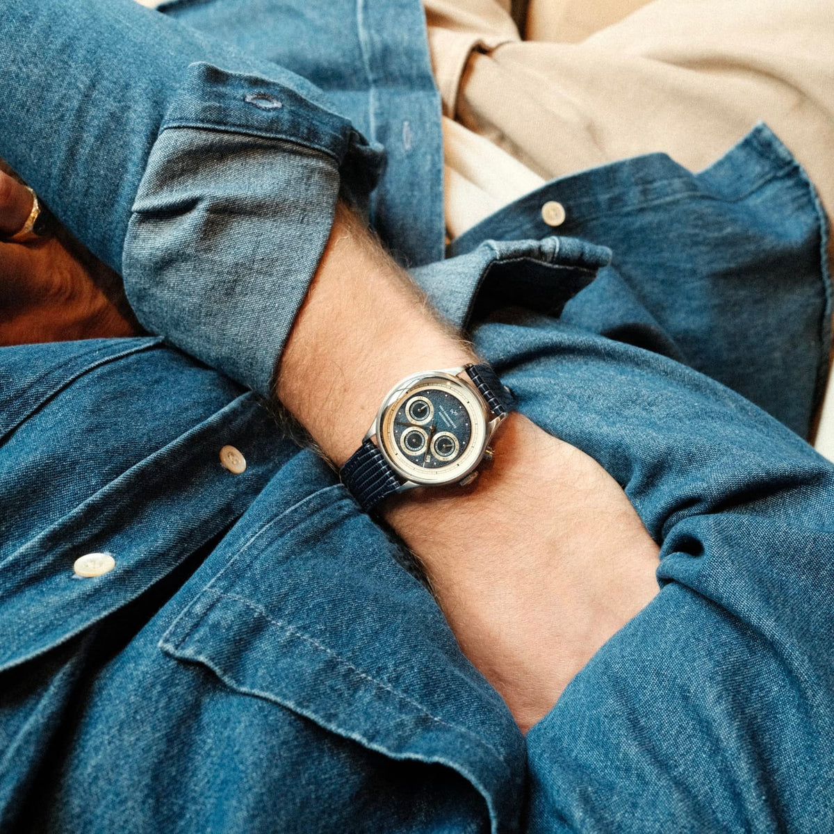 1564 Chronodate Automatic by AV86 features a vintage-inspired automatic chronograph with a blue dial, three subdials, sapphire crystal, polished steel case, and a textured blue leather strap, worn casually with denim layering reflecting refined Scandinavian design and Nordic minimalism.