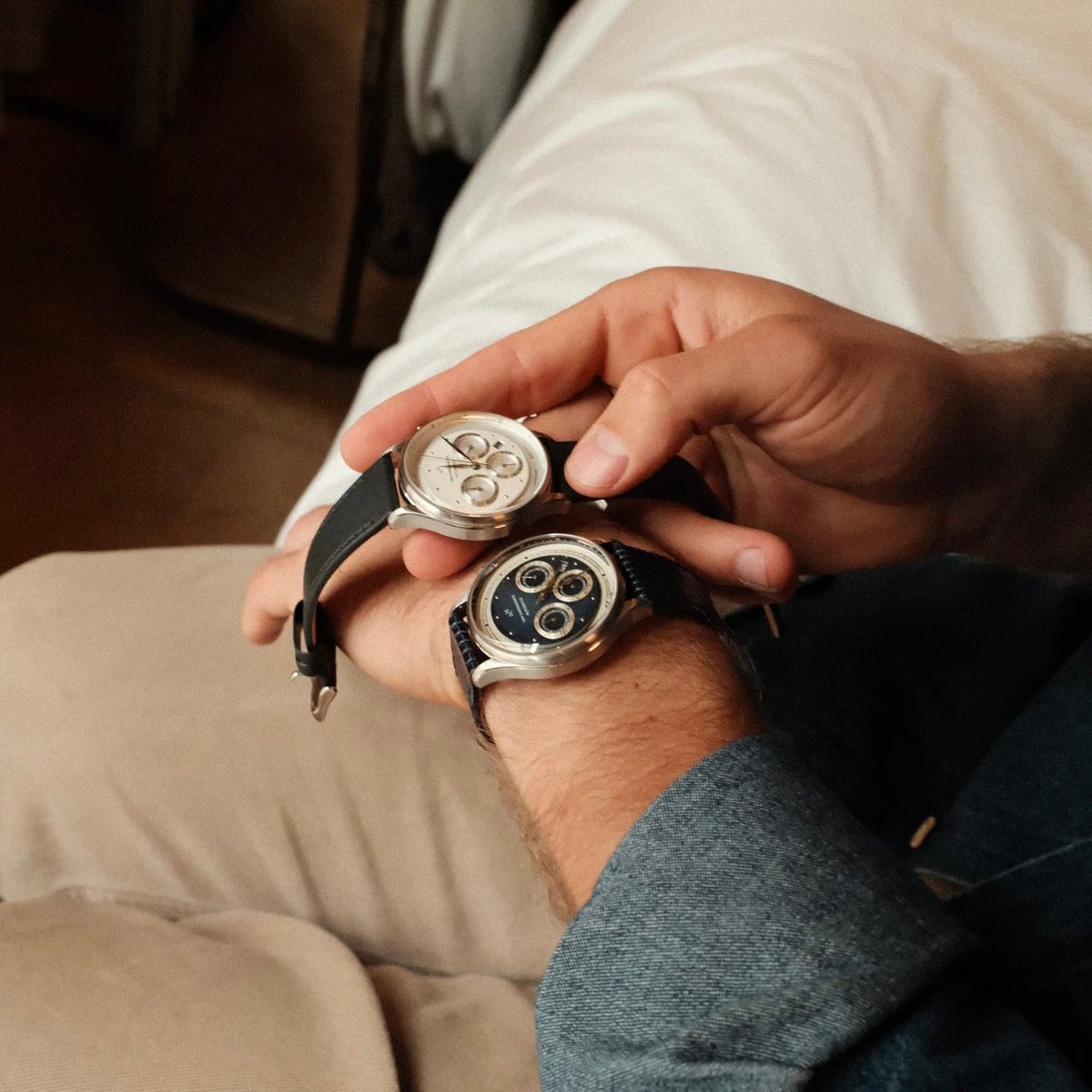 A man in casual attire adjusts the 1564 Chronodate Automatic, Steel / White by AV86, a luxury vintage-inspired chronograph with sapphire crystal and a black leather strap, showcasing refined Danish design and Nordic minimalism.