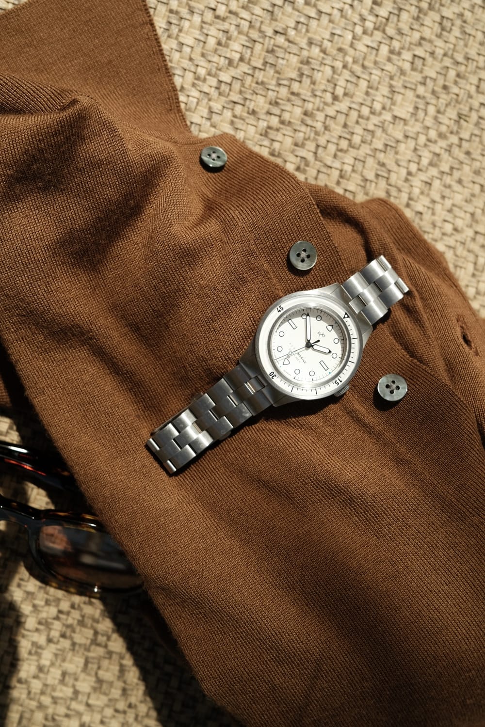 1956 Marine by AV86 luxury diver watch with sapphire crystal, rotating bezel, and brushed metal bracelet on textured fabric background