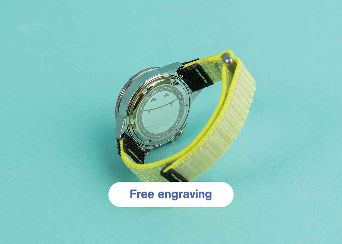 AV86 wristwatch shown from its polished caseback with a bright yellow woven strap on turquoise, above a rounded Free engraving button