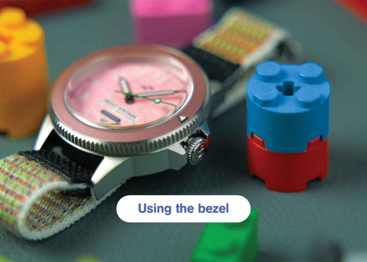 AV86 diver wristwatch with pink dial, rotating bezel and woven strap among colorful building blocks, with a rounded Using the bezel button