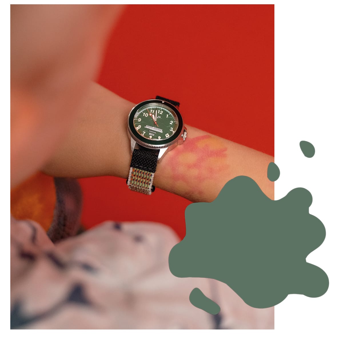 AV86 wristwatch with a green dial and black mesh strap worn against a vivid red backdrop with abstract green shapes and patterned clothing