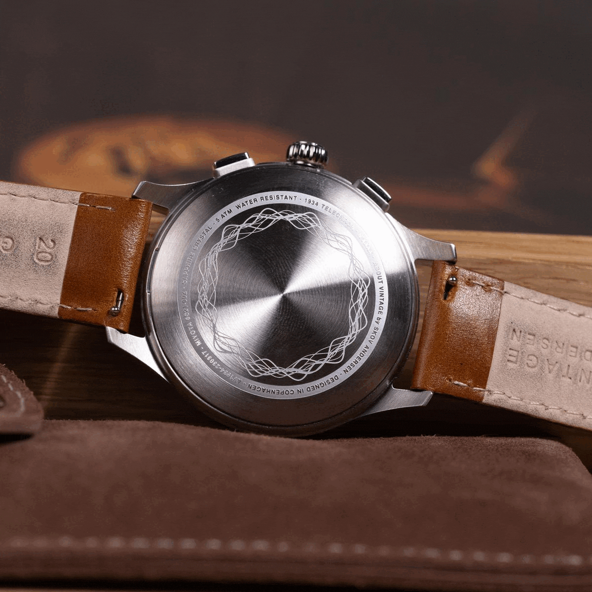 AV86 vintage-inspired chronograph viewed from the back, with an engraved caseback, brown leather strap and polished metal case resting on leather surface