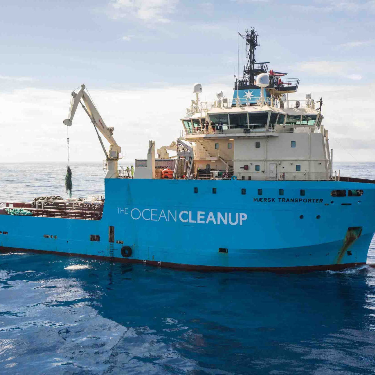 The Ocean Cleanup vessel Maersk Transporter sailing at sea with a crane lifting collected marine debris from the water