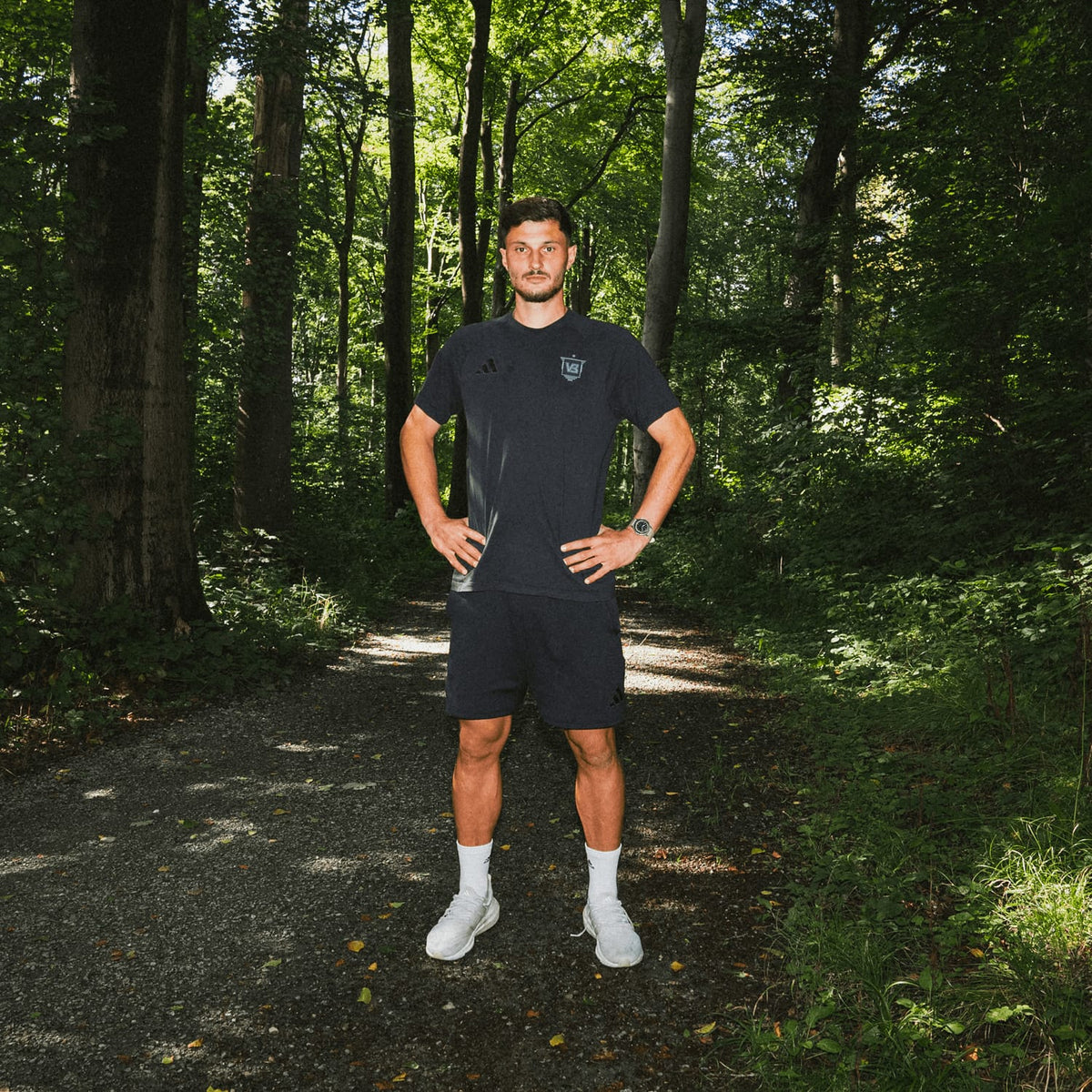 Man in casual Nordic minimalism attire stands confidently on a forest path, embodying relaxed outdoor lifestyle and natural surroundings