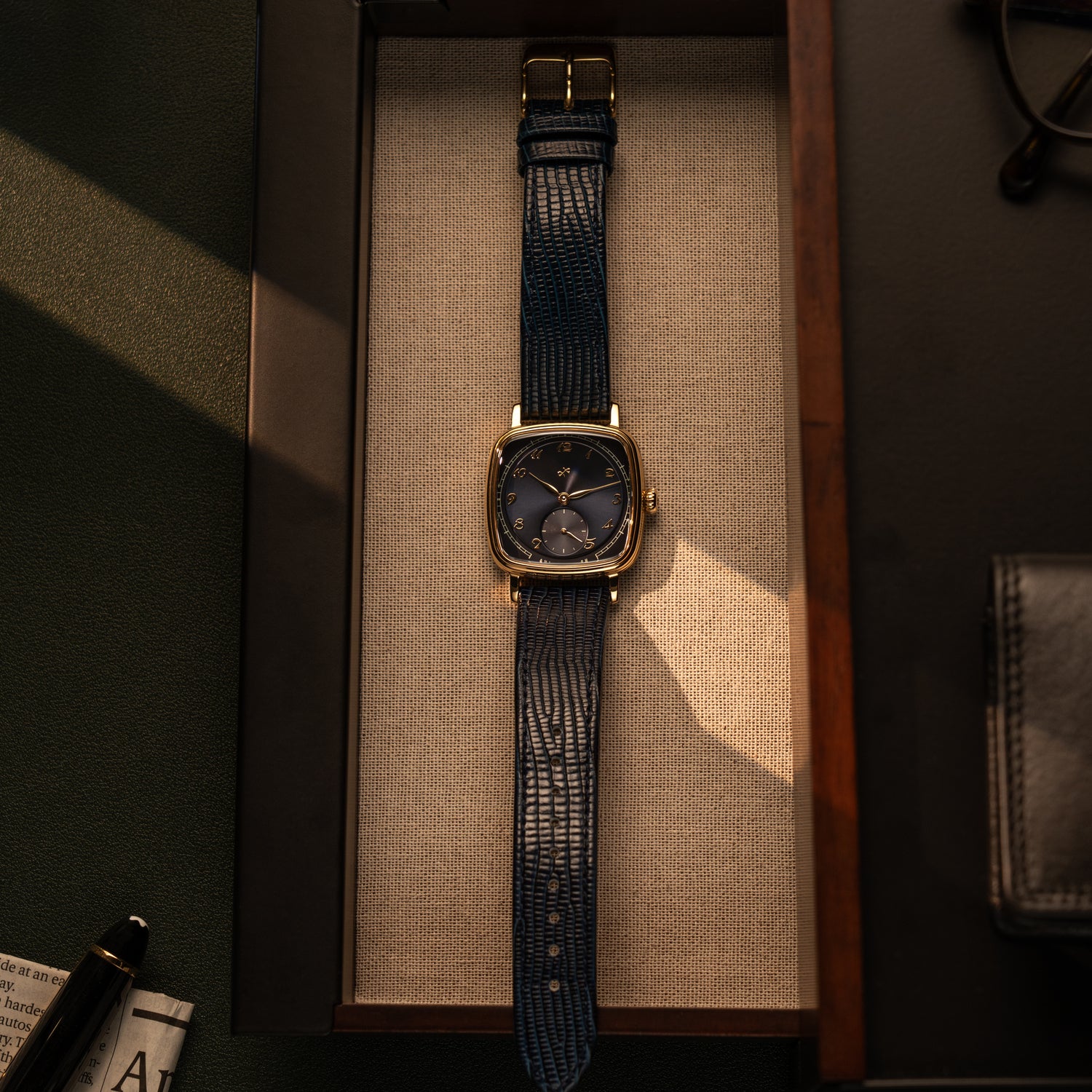 AV86 dress watch with cushion case, mechanical small seconds, textured leather strap resting in wooden tray with soft shadow play