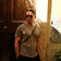 Man wearing casual muted tones and sunglasses standing in warm sunlight with Mediterranean backdrop, evoking vintage-inspired lifestyle for AV86 "1954 Amalfi Mechanical, Gold / Gold