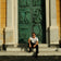 Man dressed in minimalist attire seated against ornate classical door, exuding relaxed Mediterranean style and timeless elegance wearing 1954 Amalfi Mechanical, Gold / Midnight Blue by AV86