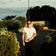 Man wearing sunglasses and a 1954 Amalfi Mechanical, Steel / Off White watch by AV86 walking outdoors near greenery and string lights.