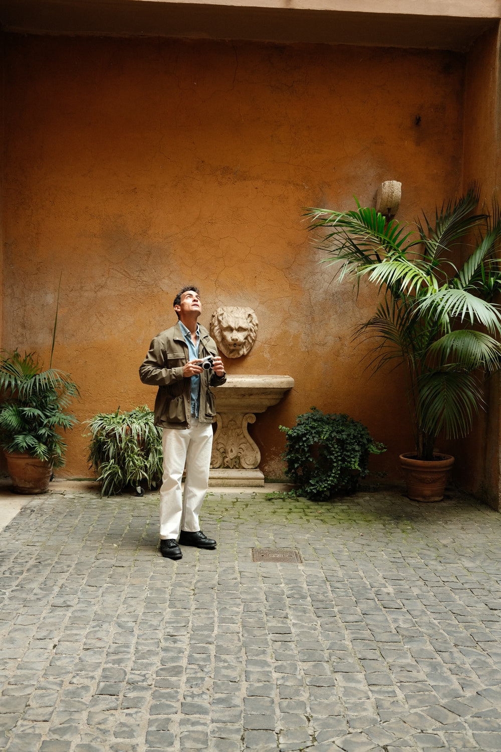 Man in casual Scandinavian outfit with 1954 Amalfi Mechanical, Gold / Midnight Blue by AV86 exploring historic Mediterranean courtyard