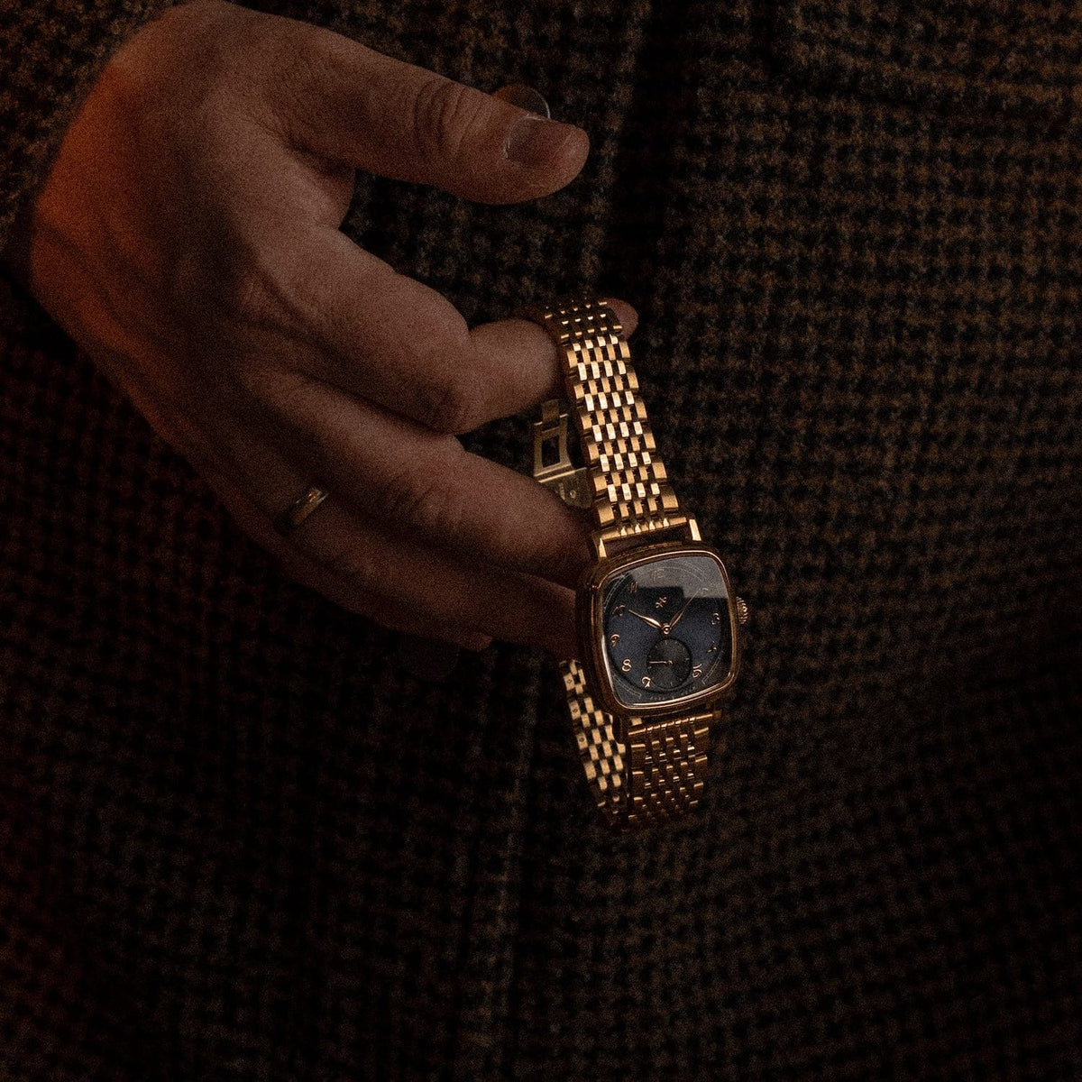 1954 Amalfi Mechanical, Gold / Midnight Blue by AV86 automatic watch with dark blue dial, gold case and bracelet held against textured fabric