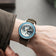 Earthrise WWF Partnership, Automatic / 2026 Edition by AV86 on wrist with a green fabric strap and blue bezel luxury timepiece.