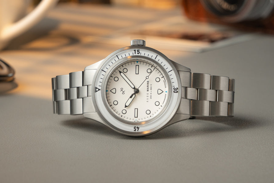 AV86 vintage-inspired diver with compass bezel, sapphire crystal, and metal bracelet strap resting on smooth surface with blurred background