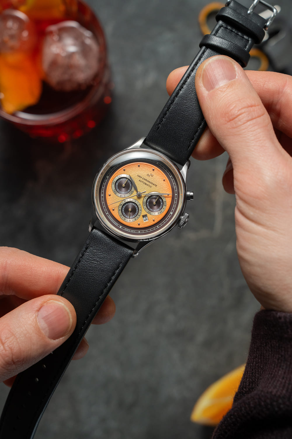 1564 Chronodate Automatic by AV86 vintage-inspired chronograph with sapphire crystal, textured dial, and black leather strap held in hand