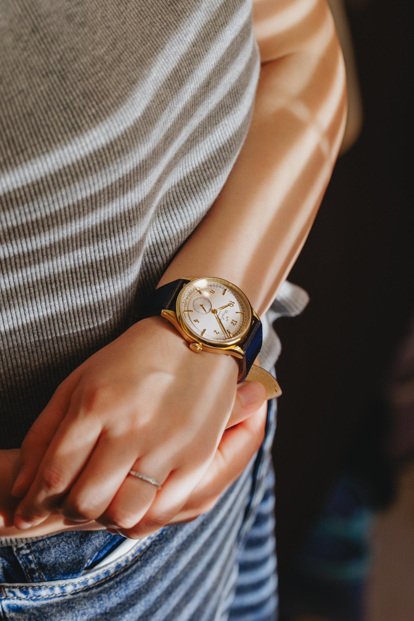 Person wearing AV86 vintage-inspired dress watch with sapphire crystal, gold case, and blue leather strap in natural light patterns